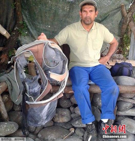 圖為當?shù)貢r間7月30日，留尼旺島上的一名海岸清潔人員展示他找到的一個手提箱的殘骸。